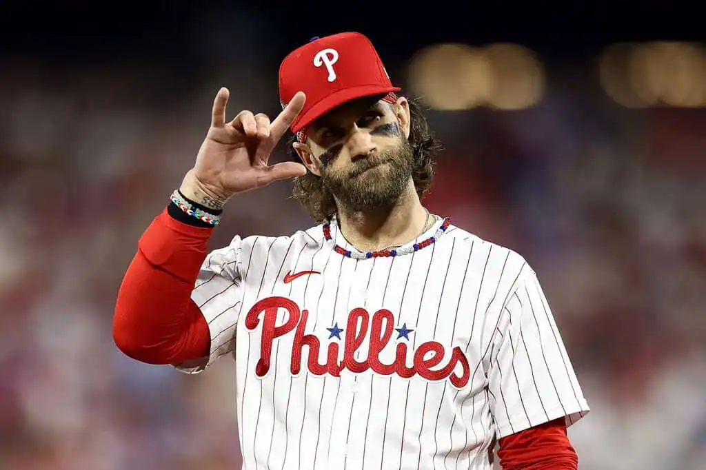 A baseball player in a red Philadelphia Phillies uniform makes a hand gesture during a game, showcasing enthusiasm and team spirit.