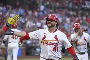 A St. Louis Cardinals player celebrates a successful play by high-fiving a teammate, with a cheering crowd in the background.