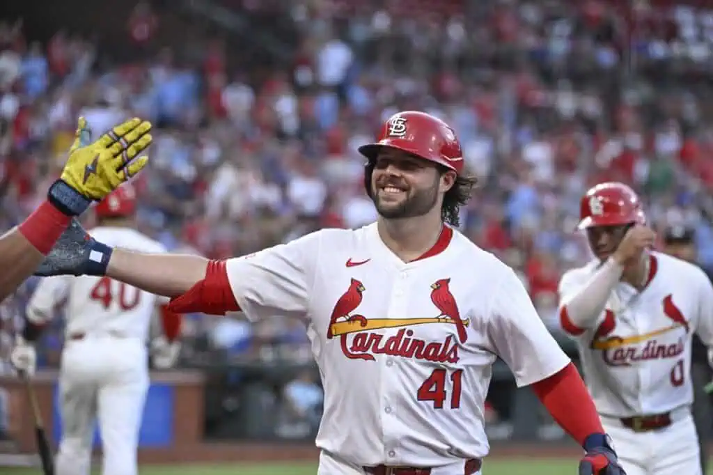 A St. Louis Cardinals player celebrates a successful play by high-fiving a teammate, with a cheering crowd in the background.