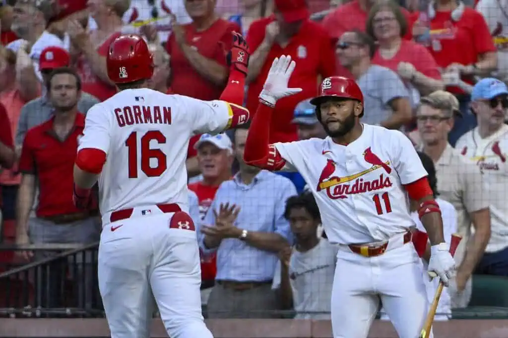 Two St. Louis Cardinals players celebrate a home run amidst an enthusiastic crowd at a baseball game, with fans in team colors.