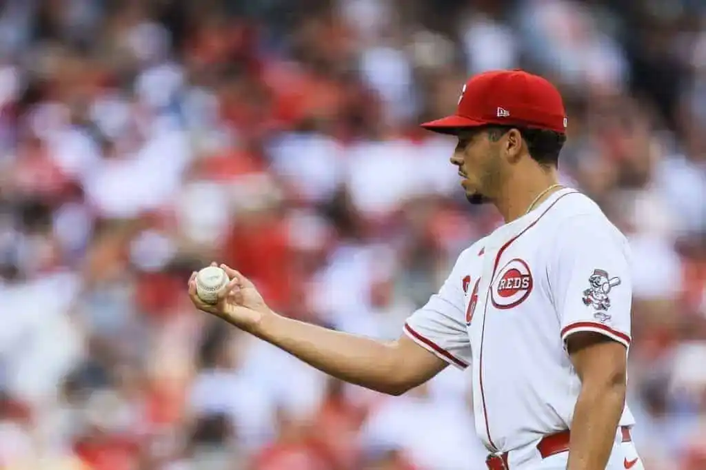 A Cincinnati Reds pitcher stands on the field holding a baseball.