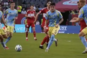 A group of soccer players in blue and yellow jerseys competes against opponents in red uniforms on a vibrant field.