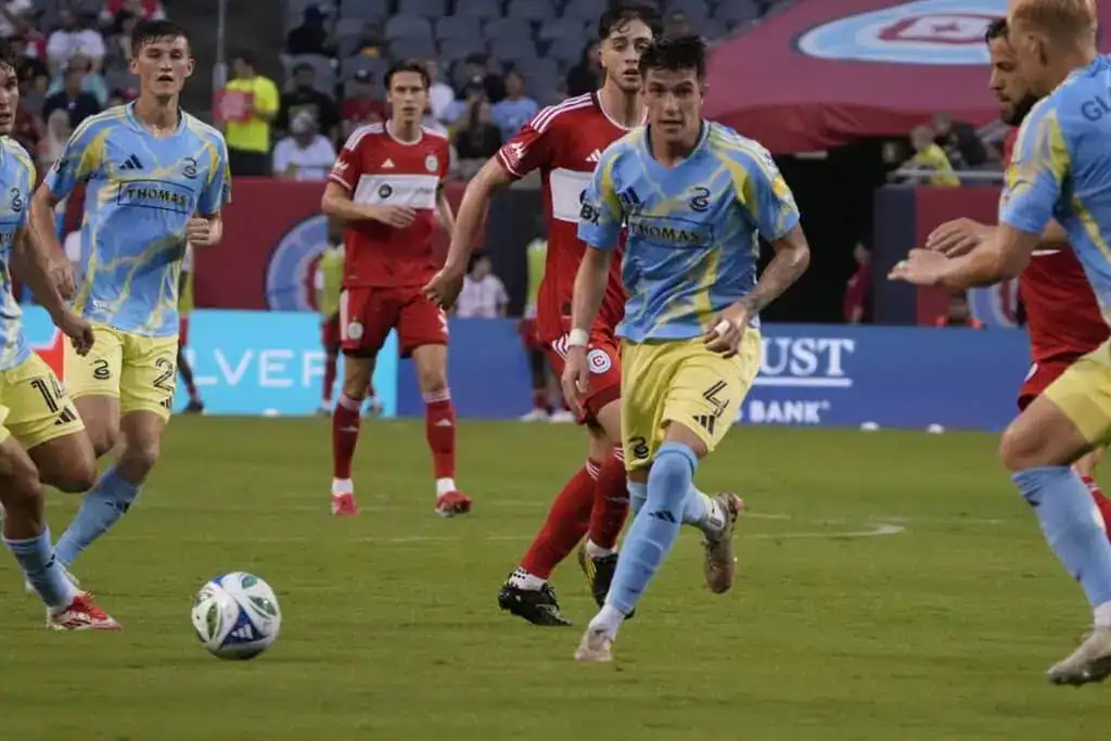 A group of soccer players in blue and yellow jerseys competes against opponents in red uniforms on a vibrant field.