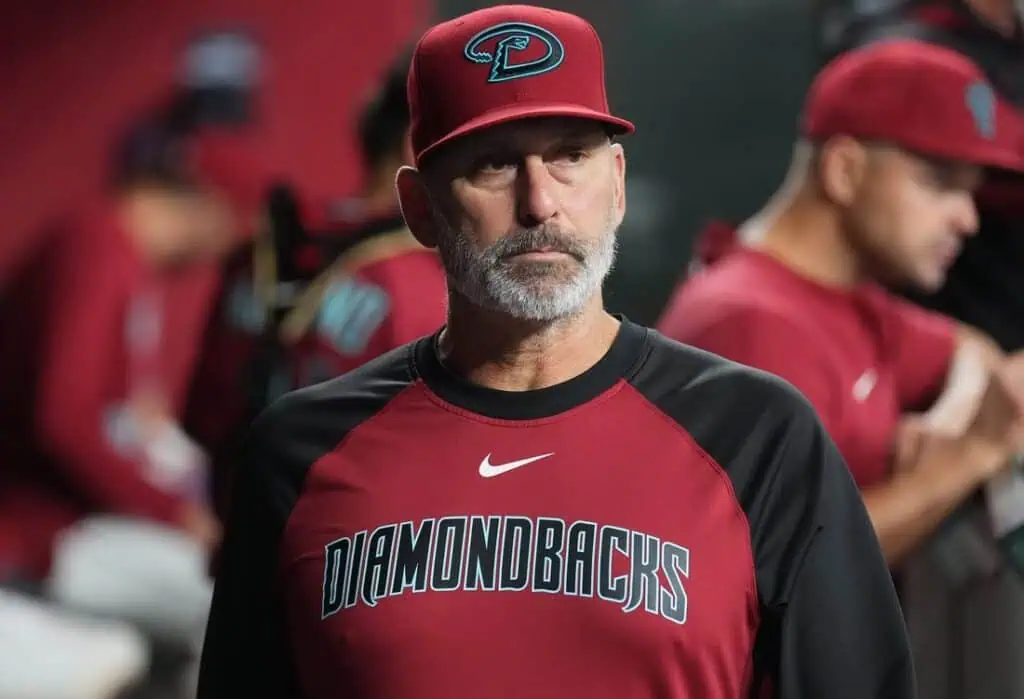 A man in a red and black Arizona Diamondbacks jersey stands in a baseball dugout