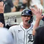 A baseball player in a white jersey celebrating with teammates, exchanging high-fives in a lively stadium atmosphere.
