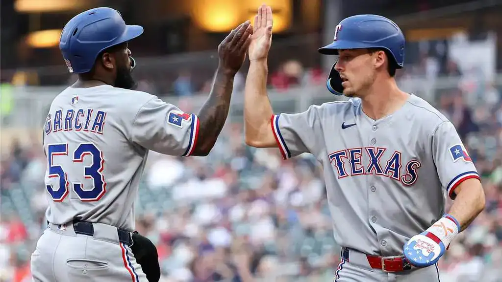 Texas Rangers vs Chicago White Sox Picks and Predictions June 15th 2025 2 Two Texas Rangers players celebrate together with a high five on the baseball field, wearing gray uniforms adorned with team logos.