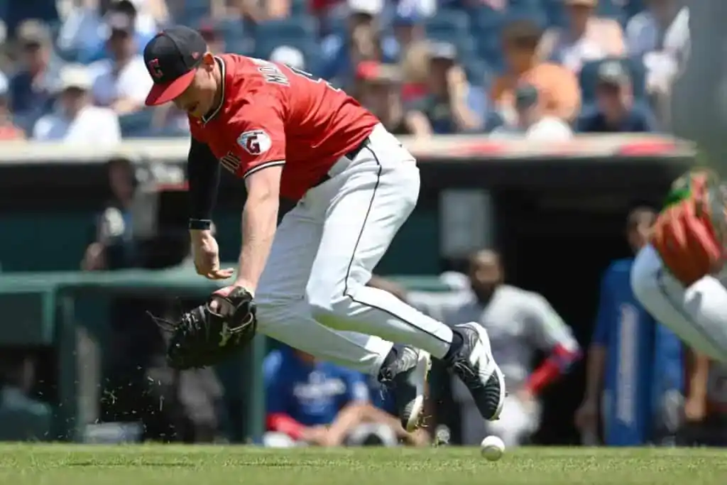 A Cleveland Guardians player in a red jersey dives towards a baseball on the grass.