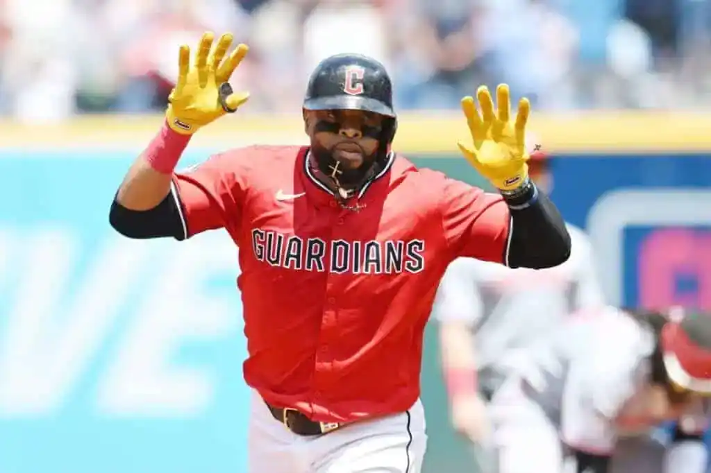 A baseball player in a red Guardians jersey celebrates, raising his hands in excitement during a game on a sunny day.