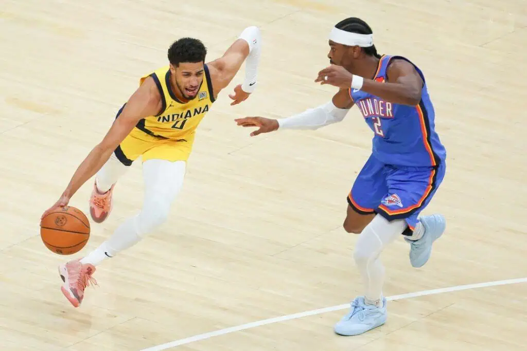 A player in a yellow Indiana jersey dribbles a basketball while being closely defended by a player in a blue Thunder uniform.