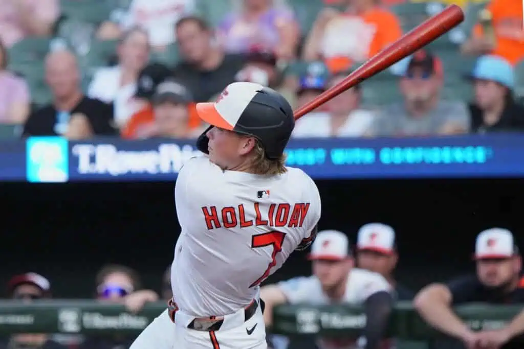 A baseball player in a white jersey with "Holliday" and the number 7 prepares to swing a bat at a game, with fans in the background.