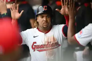 A baseball player in a white jersey with "Guardians" logo celebrates, raising both hands in excitement among teammates.