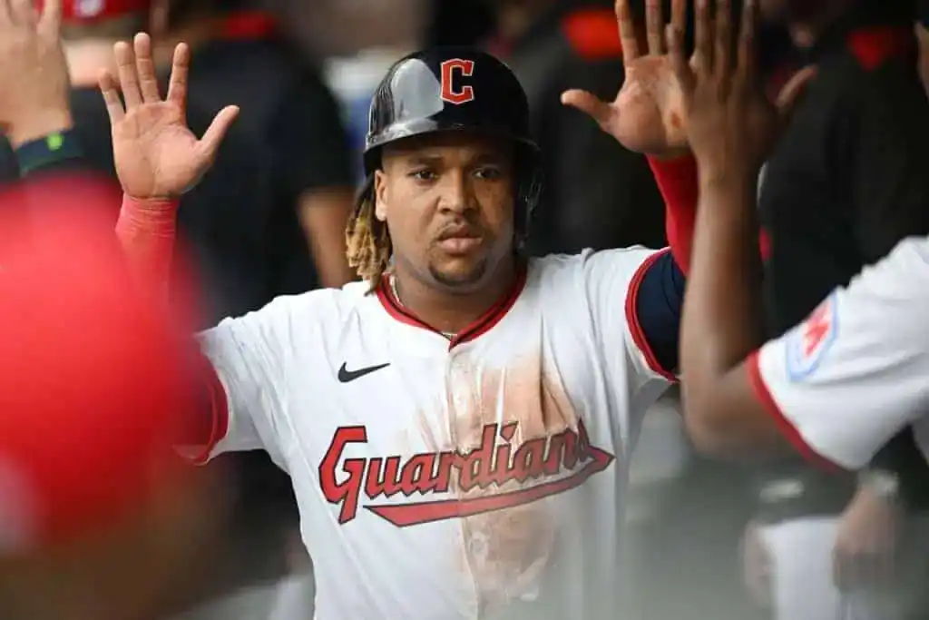 A baseball player in a white jersey with "Guardians" logo celebrates, raising both hands in excitement among teammates.