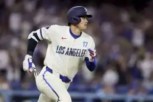 A baseball player in a white uniform with "LOS ANGELES" printed runs energetically on the field during a game, surrounded by fans.