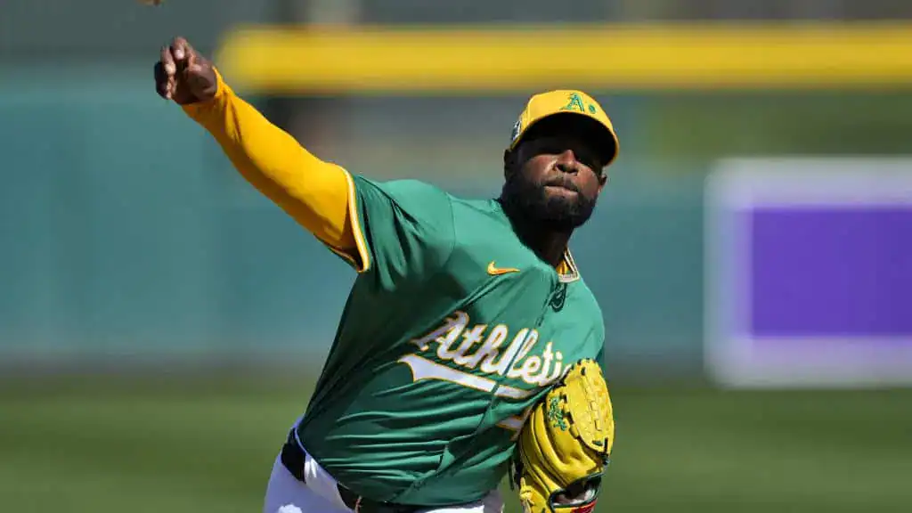 An Oakland Athletics pitcher in a green and yellow uniform throws a pitch during a game.