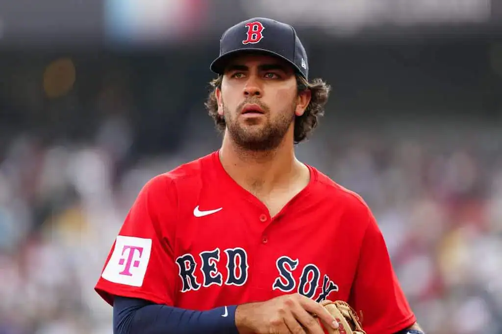 Boston Red Sox vs New York Yankees Picks and Predictions June 13th 2025 2 A Boston Red Sox player in a red jersey stands on the field, holding a baseball glove, with a blurred crowd in the background.
