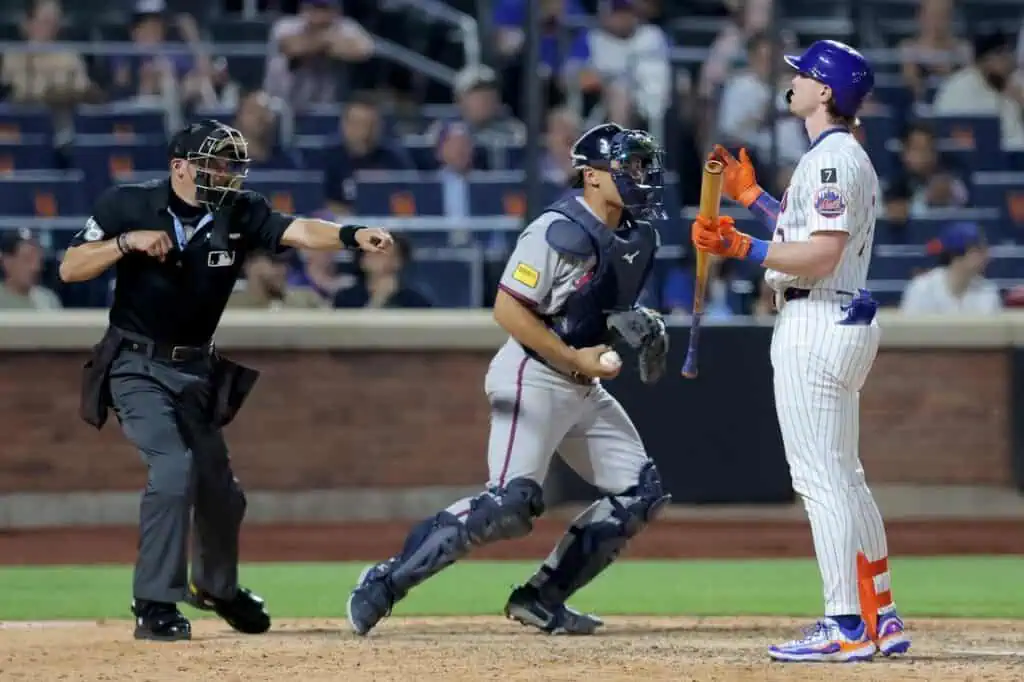 A baseball catcher prepares to throw while the umpire signals, and a batter stands ready, following a tense moment during the game.