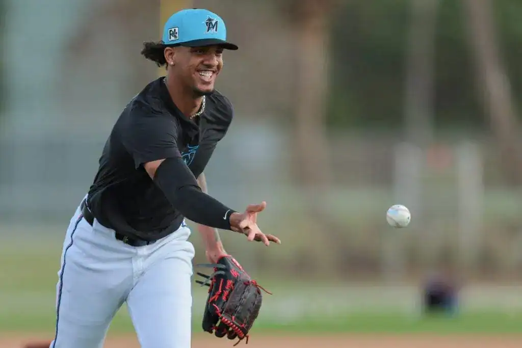 3 A player wearing a black shirt and white pants prepares to catch a baseball during practice, with palm trees in the background.