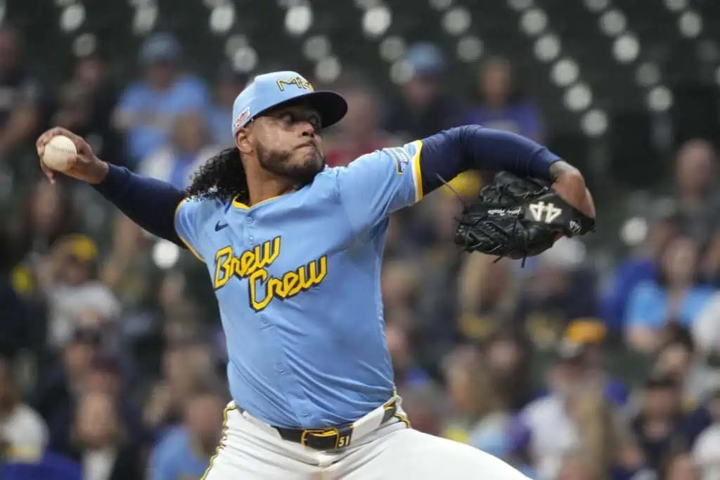 A baseball pitcher in a light blue "Brew Crew" jersey prepares to deliver a pitch