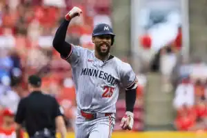 A Minnesota baseball player in a gray uniform celebrates excitedly after a play, with a blurred crowd of spectators in the background.