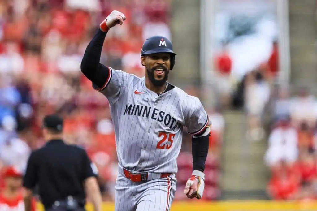 A Minnesota baseball player in a gray uniform celebrates excitedly after a play, with a blurred crowd of spectators in the background.