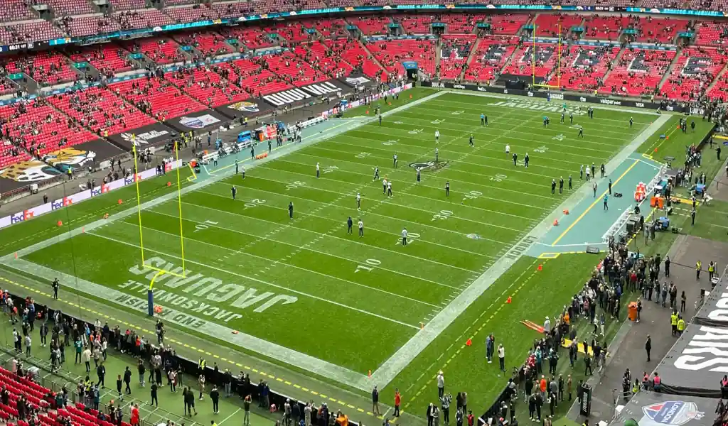 NFL teams warming up on the field ahead of a game, with stadium crowd gathering