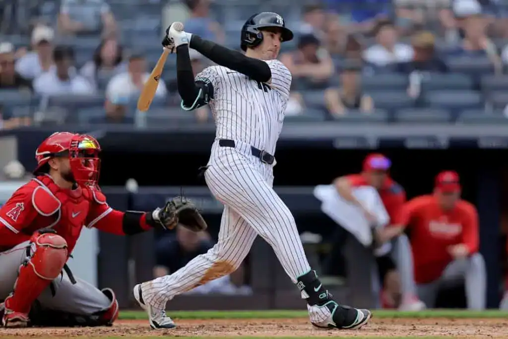 A baseball player swings a bat during a game, while a catcher in red gear crouches behind home plate.