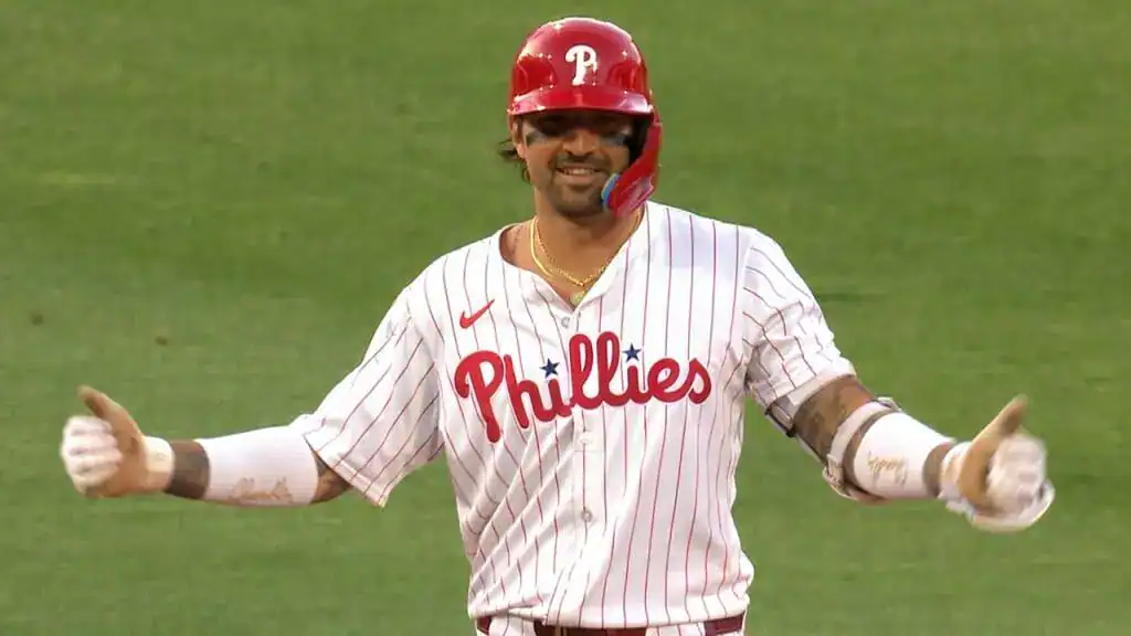 Miami Marlins vs Philadelphia Phillies Picks and Predictions June 18th 2025 2 A baseball player in red helmet and pinstriped jersey with "Phillies" logo stands with arms open, conveying excitement during a game.
