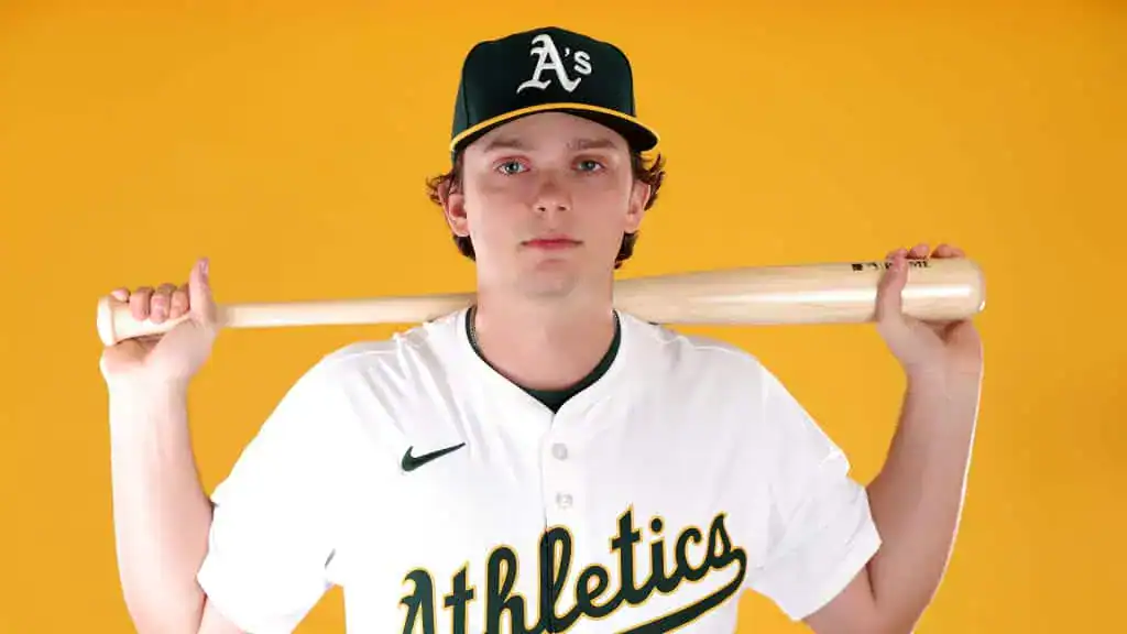 Oakland Athletics vs Houston Astros Picks and Predictions June 16th 2025 2 A person in a white and green Athletics baseball uniform holds a wooden bat over their shoulder against a bright yellow background.