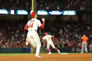 A baseball player in a white jersey with red accents celebrates as he rounds the bases, while a teammate heads to first base behind him.
