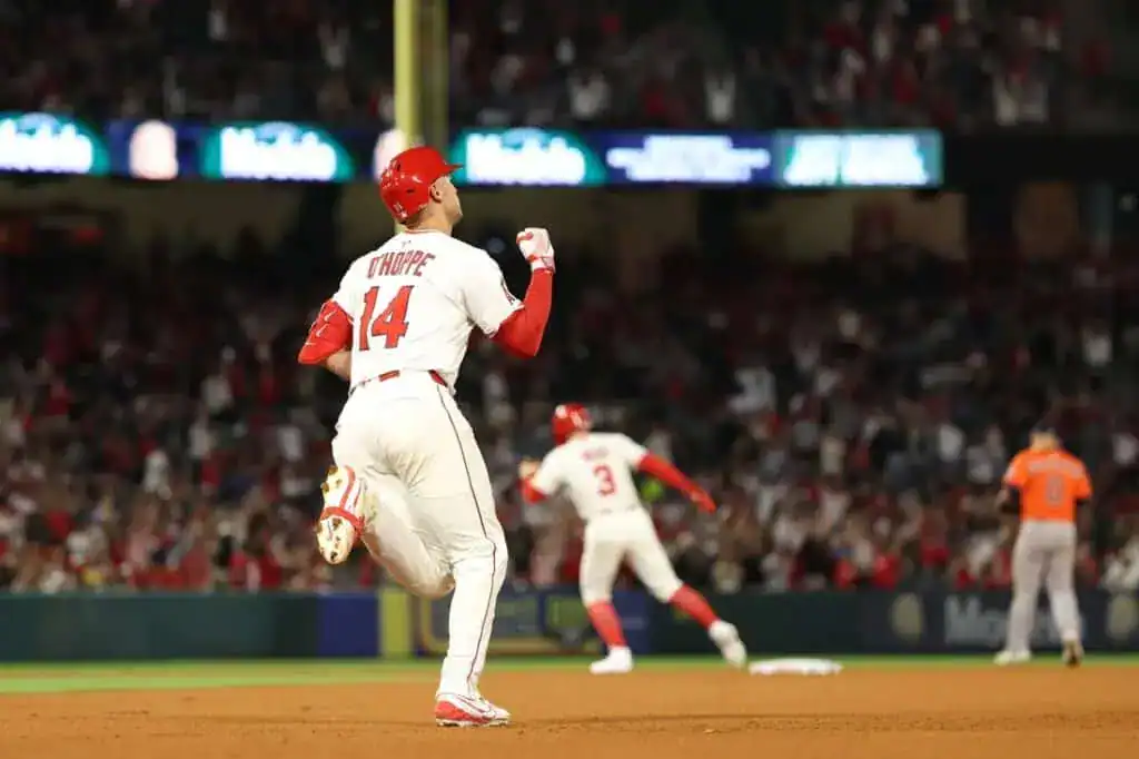 A baseball player in a white jersey with red accents celebrates as he rounds the bases, while a teammate heads to first base behind him.