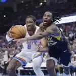 Two basketball players compete for the ball during a game, with one player in a white uniform holding the ball and the other in a dark uniform defending closely.