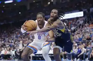 Two basketball players compete for the ball during a game, with one player in a white uniform holding the ball and the other in a dark uniform defending closely.