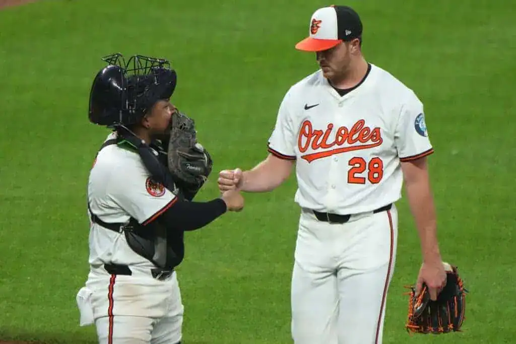 A Baltimore Orioles pitcher and catcher fist bump on the field during a game.