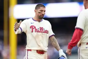A Philadelphia Phillies player celebrates with teammates, wearing a home jersey, showing excitement after a successful play on the field.