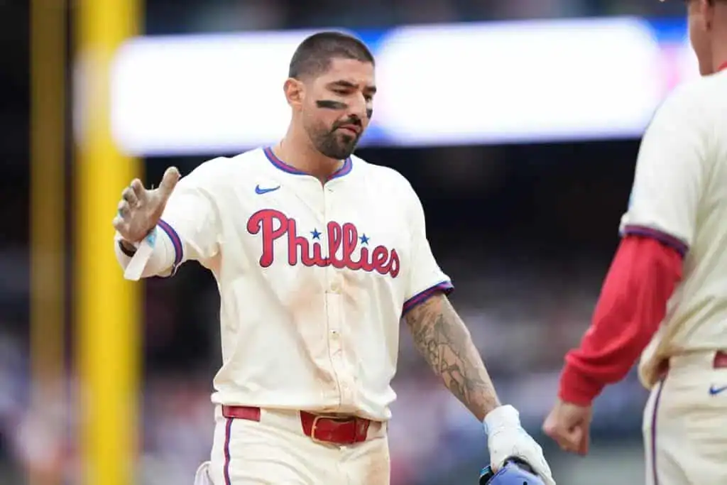 A Philadelphia Phillies player celebrates with teammates, wearing a home jersey, showing excitement after a successful play on the field.