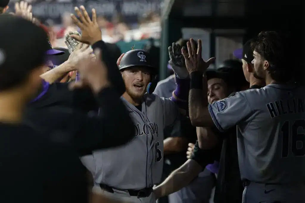 A group of Colorado Rockies players celebrate in the dugout, giving each other high-fives after a successful play.