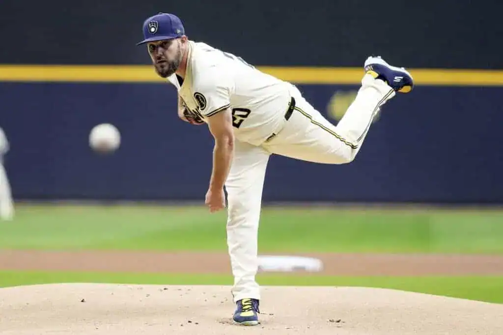 4 A pitcher in a cream baseball uniform winds up on the mound, preparing to throw a pitch, with the ball in mid-air.