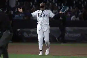 A baseball player in a Rays uniform stands on the field, arms outstretched in celebration or excitement, under stadium lights.