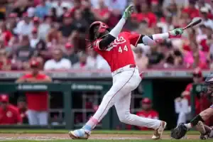 A baseball player in a red uniform swings a bat while playing at a crowded stadium, showcasing a moment of action during a game.
