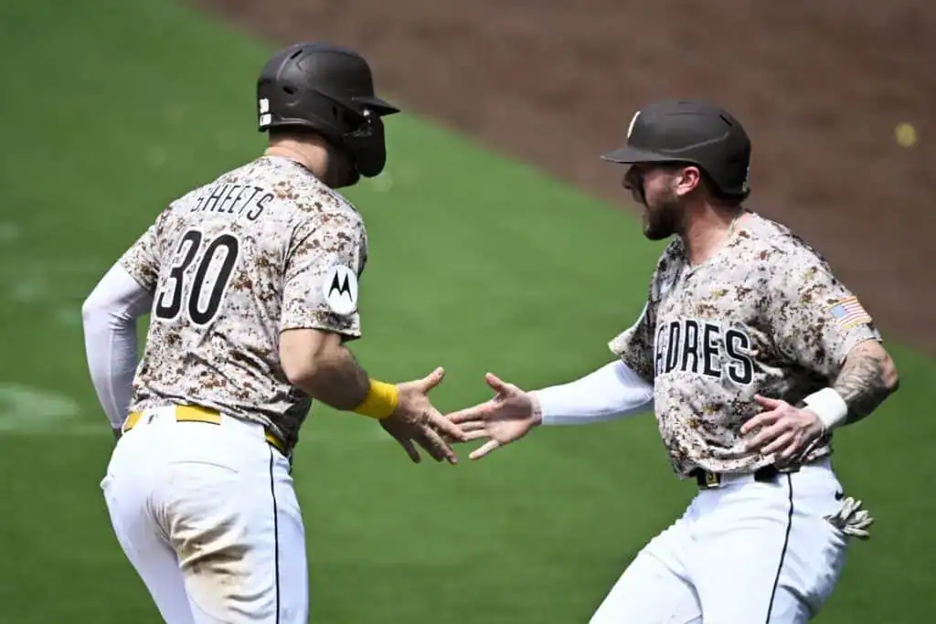 Two baseball players in camouflage jerseys celebrate with a high-five on the field