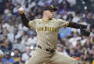 A San Diego Padres pitcher winds up to throw a baseball, wearing a tan and brown striped uniform, with a crowded stadium in background.