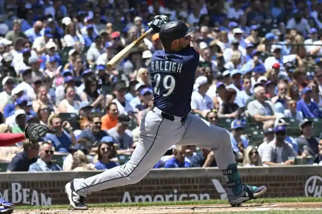 A baseball player in a navy jersey swings a bat in a packed stadium,