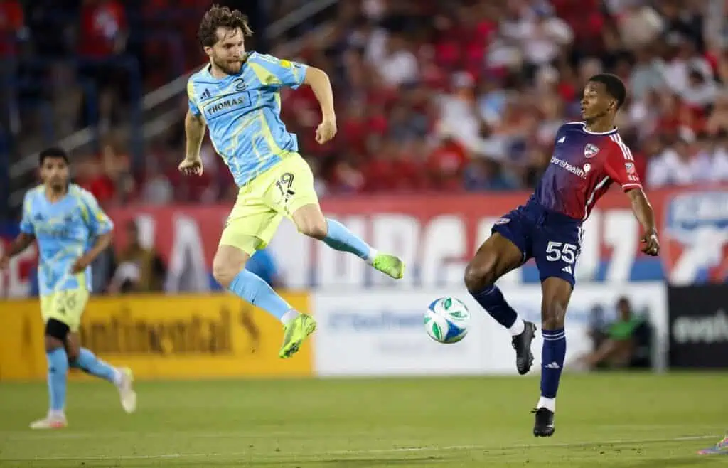 A soccer match in progress with players in colorful jerseys competing for the ball on a lively field, surrounded by enthusiastic fans.