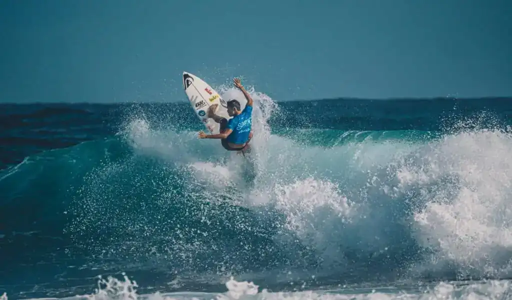 Surfista ejecutando una maniobra en una gran ola, representando el surf masculino en París 2024. Tamaño: 1024x600 px