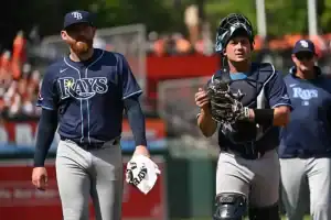 Three Tampa Bay Rays players in navy blue jerseys walk on a baseball field.
