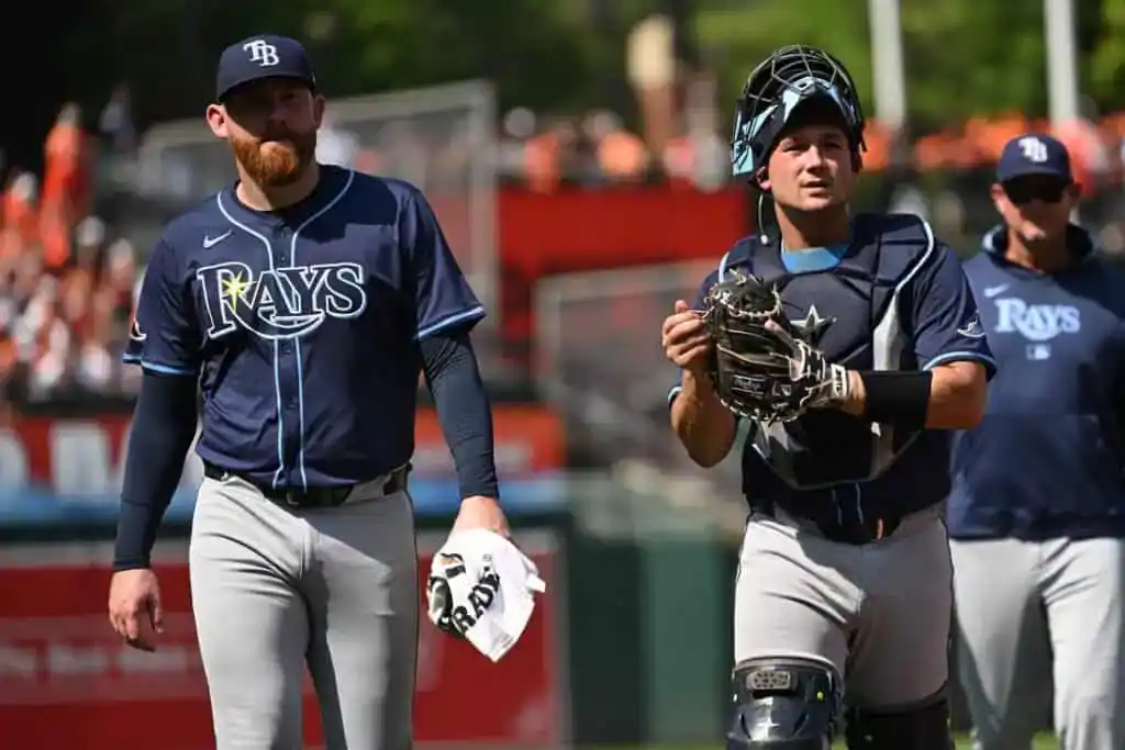Three Tampa Bay Rays players in navy blue jerseys walk on a baseball field.