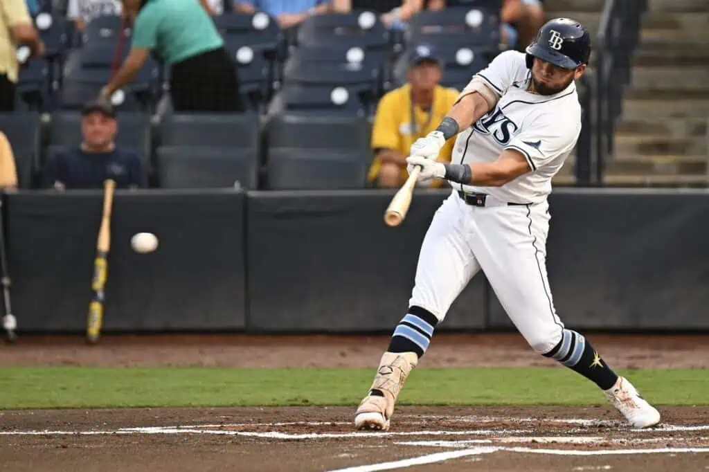 A baseball player in a white uniform swings a bat, aiming to hit a pitched ball during a game, surrounded by spectators.