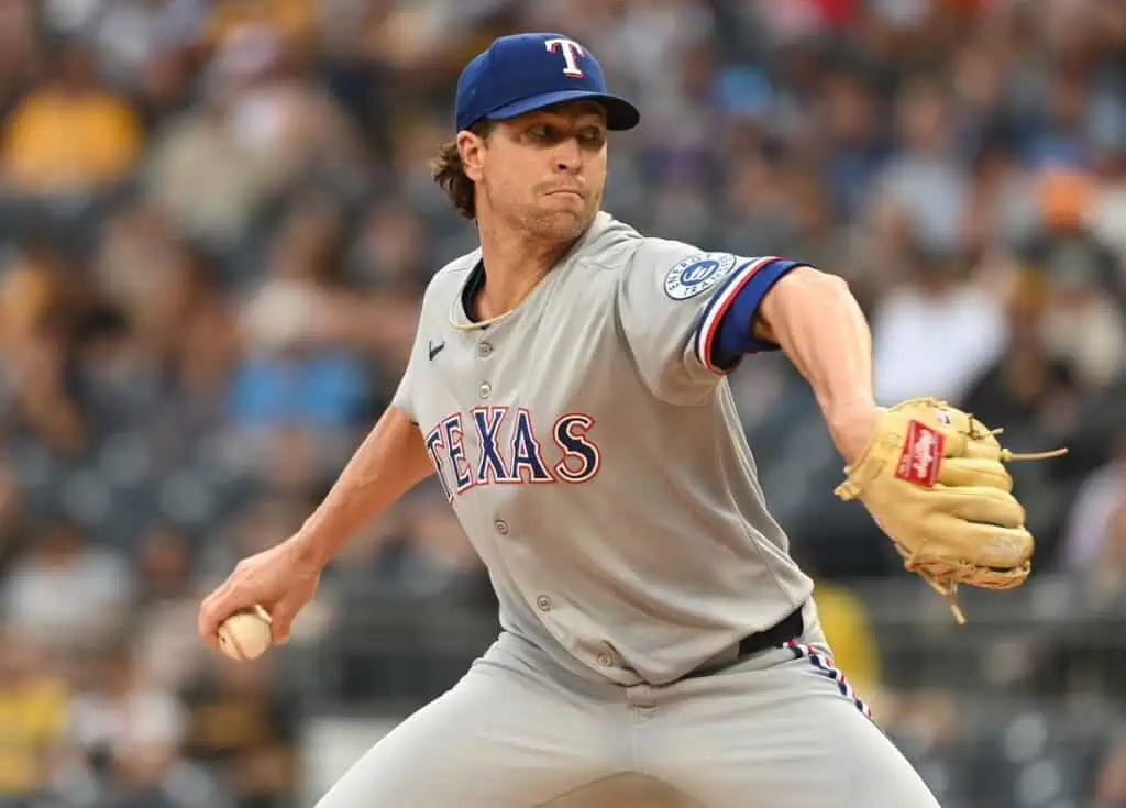 A Texas Rangers pitcher in gray uniform winds up to throw a baseball during a game.