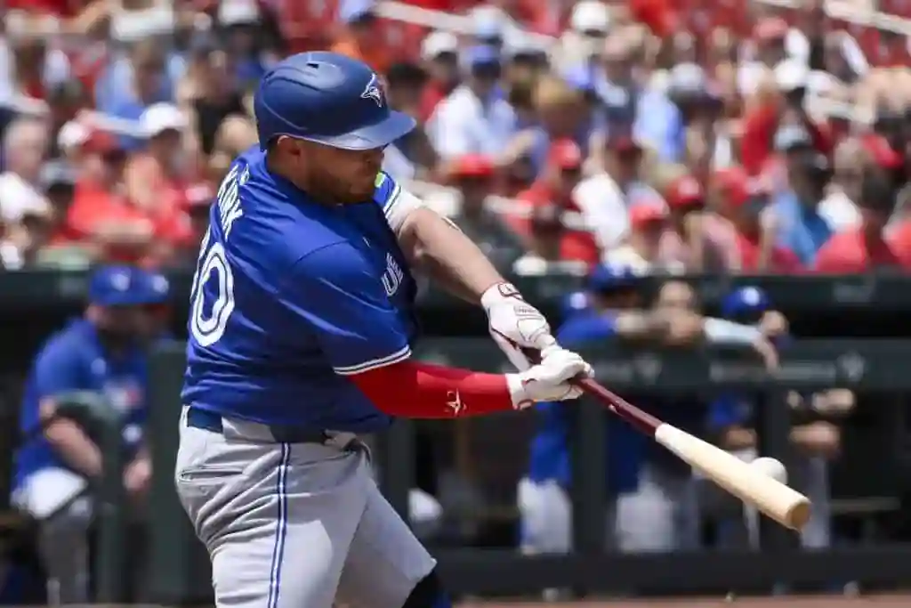 A baseball player in a blue jersey swings a bat during a game, surrounded by a cheering crowd in red and blue attire.