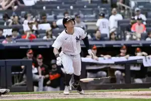 A baseball player in a striped Yankees uniform swings a bat, with the crowd and team members